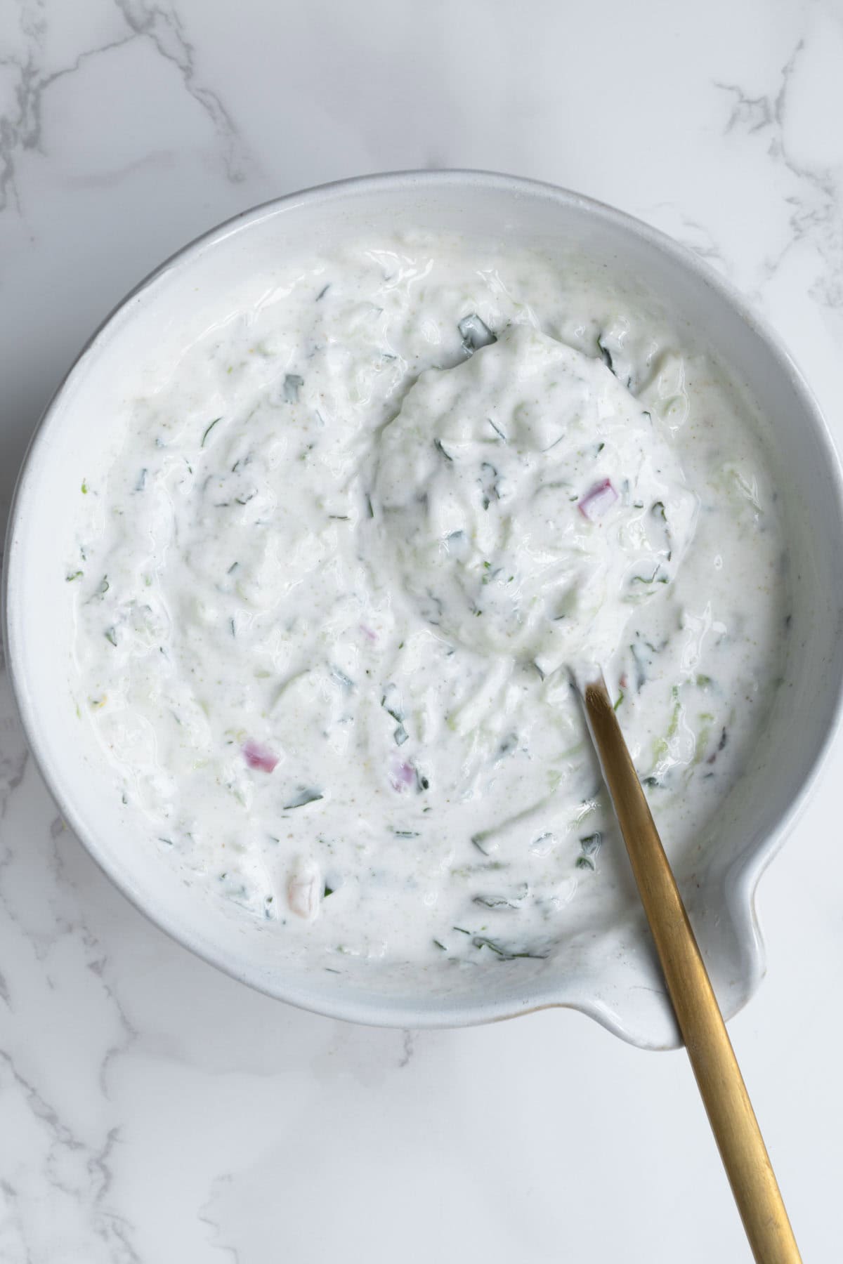 High-protein raita in white bowl with a gold spoon.