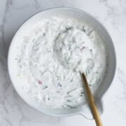 High-protein raita in white bowl with a gold spoon.
