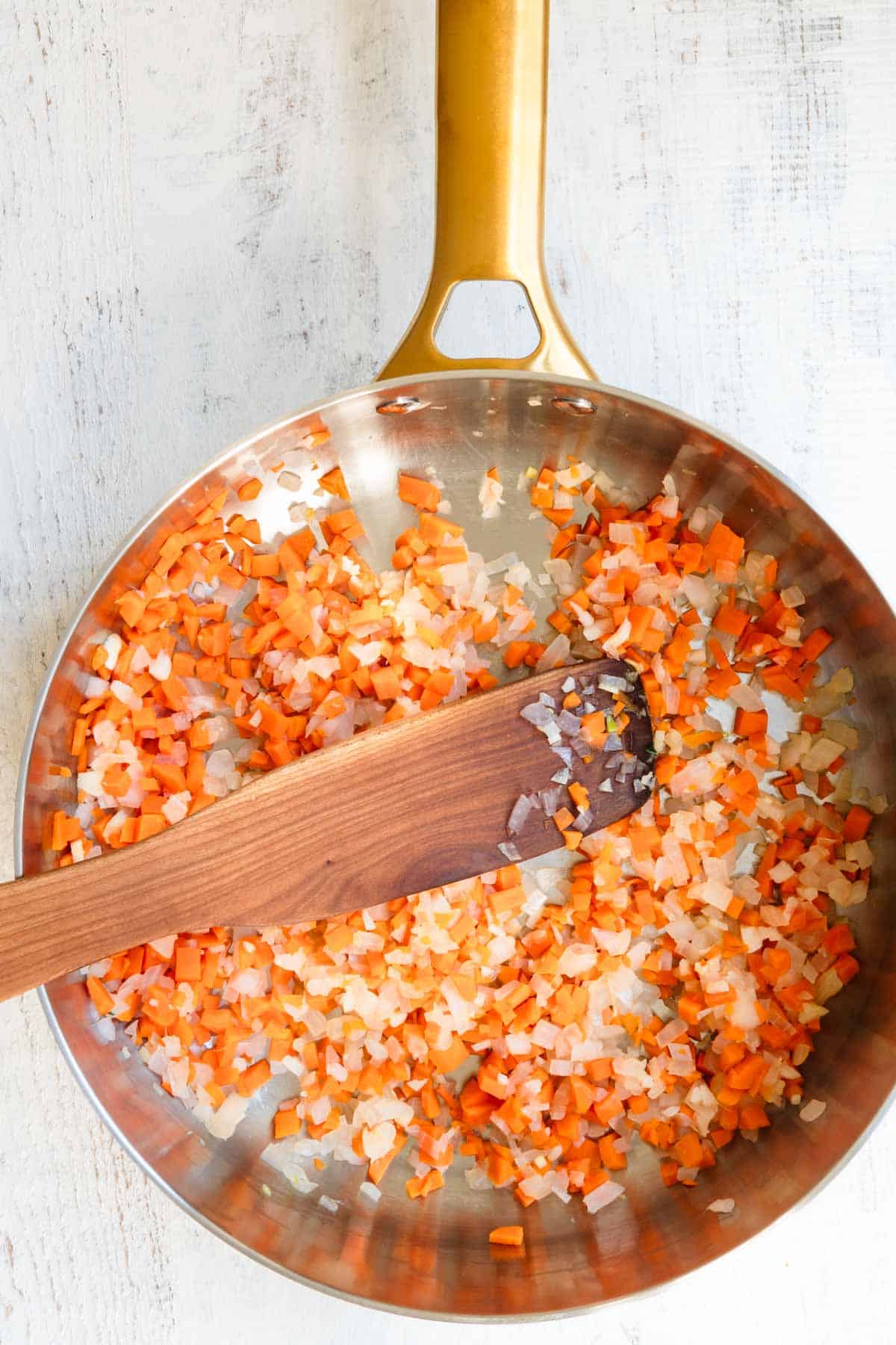 Chopped onion and carrot cooked in a stainless saucepan.
