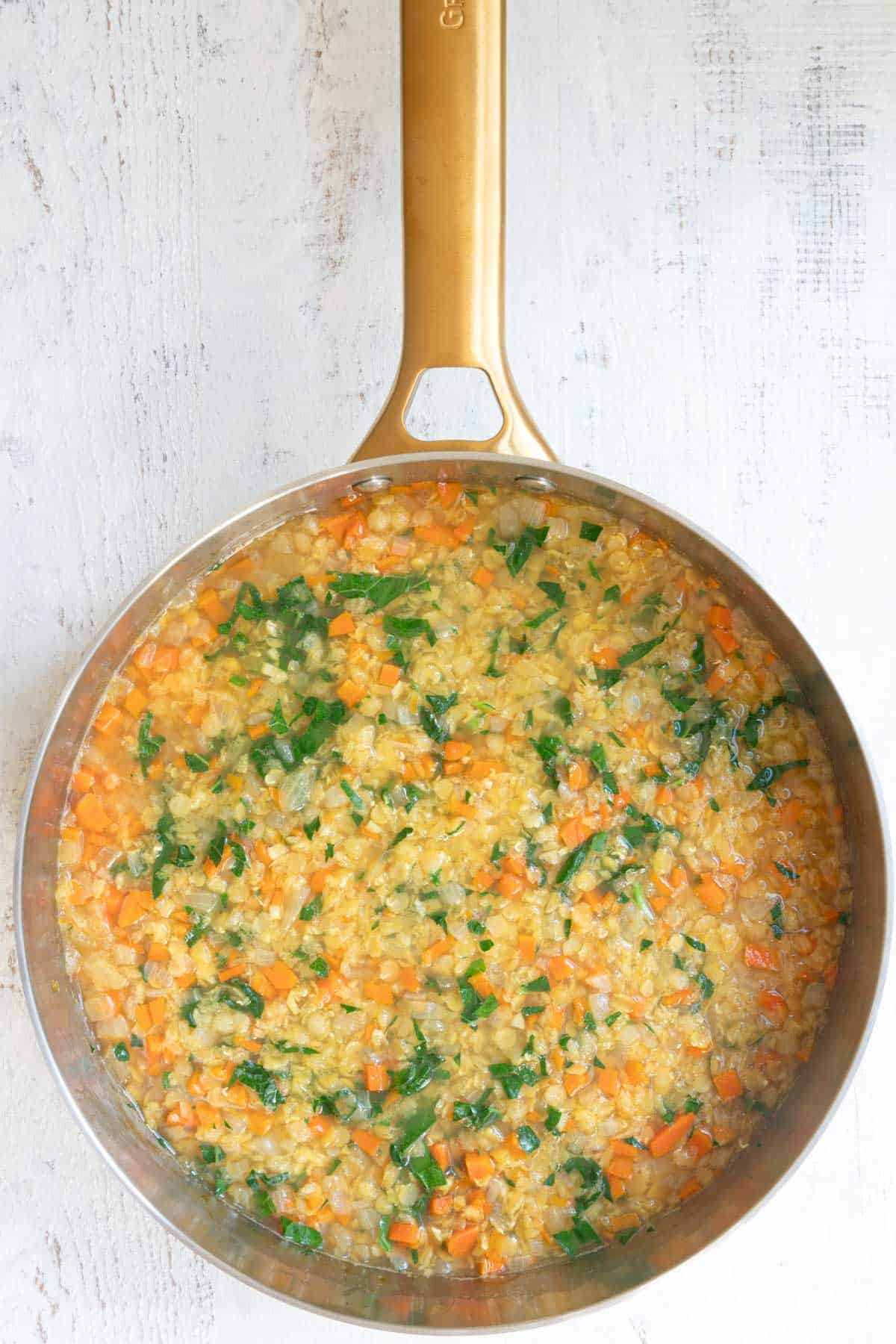 Cooked red lentil soup with kale in a stainless saucepan.