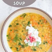 Red lentil soup in a bowl topped with raita and chopped red lentils.