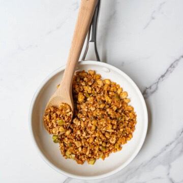Tofu crumbles cooked in a white saucepan with a wooden spoon.