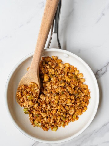 Tofu crumbles cooked in a white saucepan with a wooden spoon.