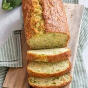 Vegan zucchini bread on a wooden cutting board with a green napkin and zucchini.