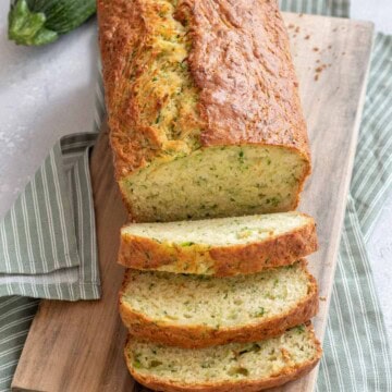 Vegan zucchini bread on a wooden cutting board with a green napkin and zucchini.