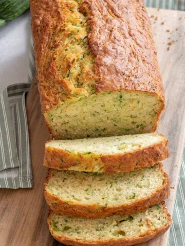 Vegan zucchini bread on a wooden cutting board with a green napkin and zucchini.