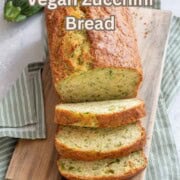 Vegan zucchini bread on a wooden cutting board with a green napkin and zucchini.