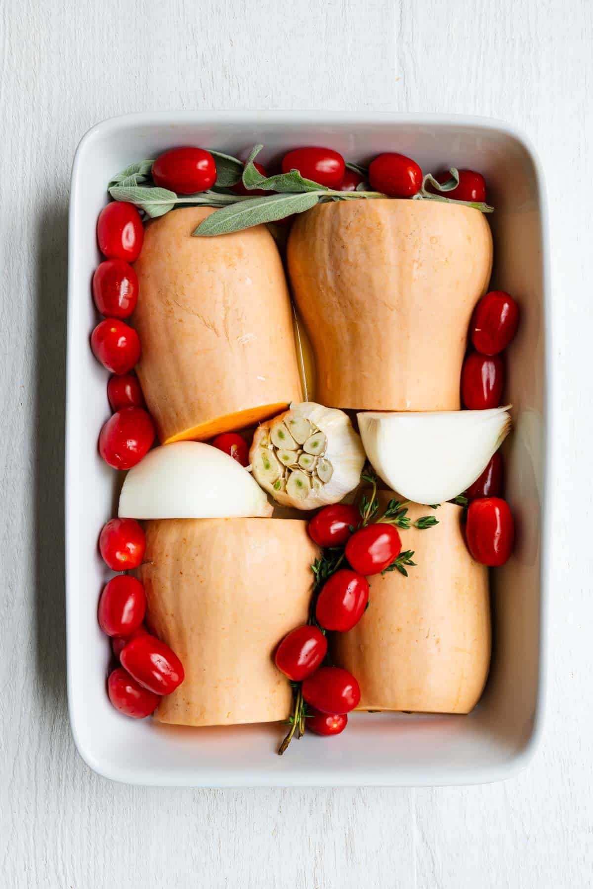 Roasted butternut squash, cherry tomatoes, garlic, onion, and fresh herbs with broth in a baking dish.