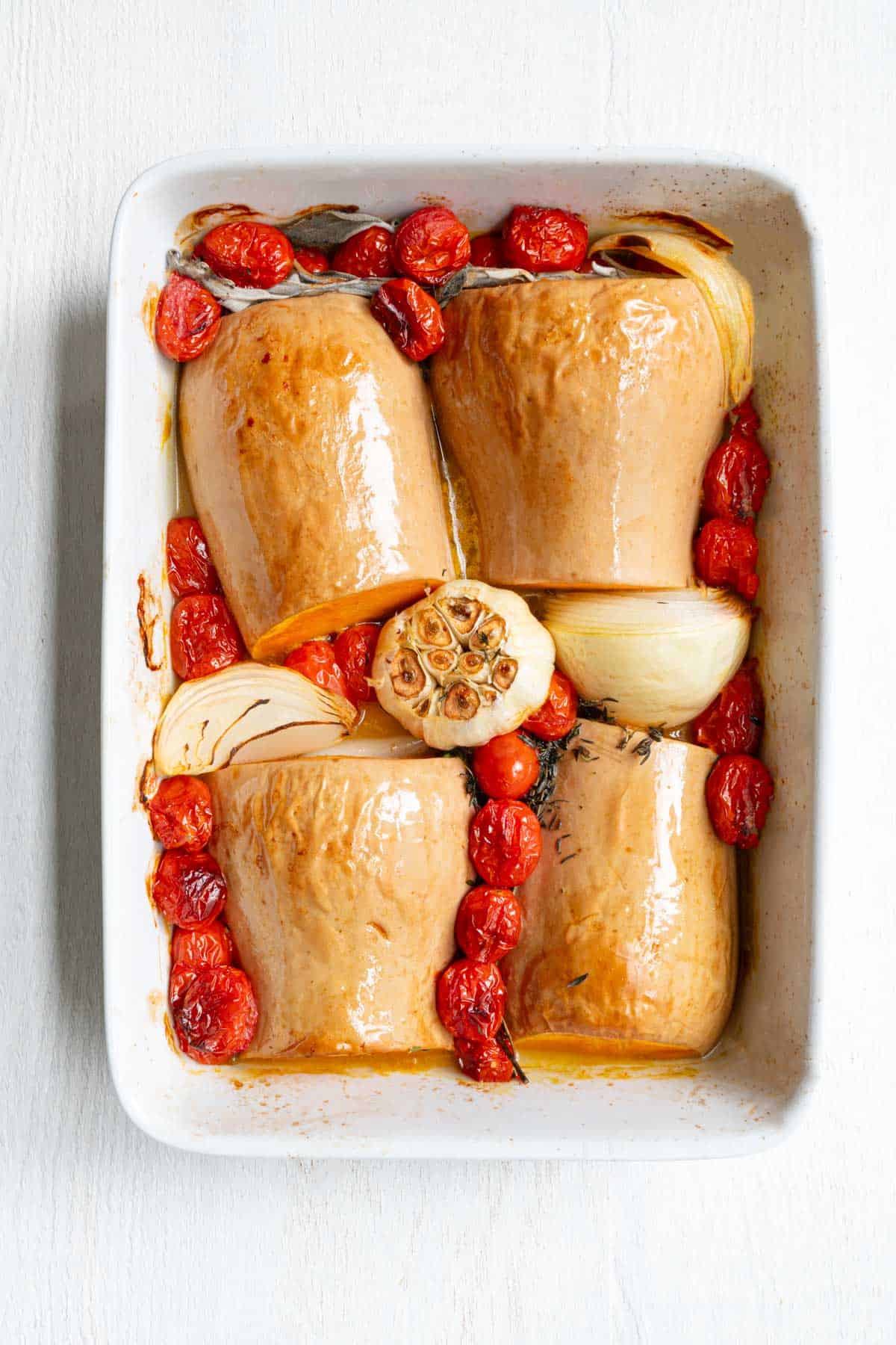 Roasted butternut squash, cherry tomatoes, garlic, onion, and fresh herbs in a baking dish.