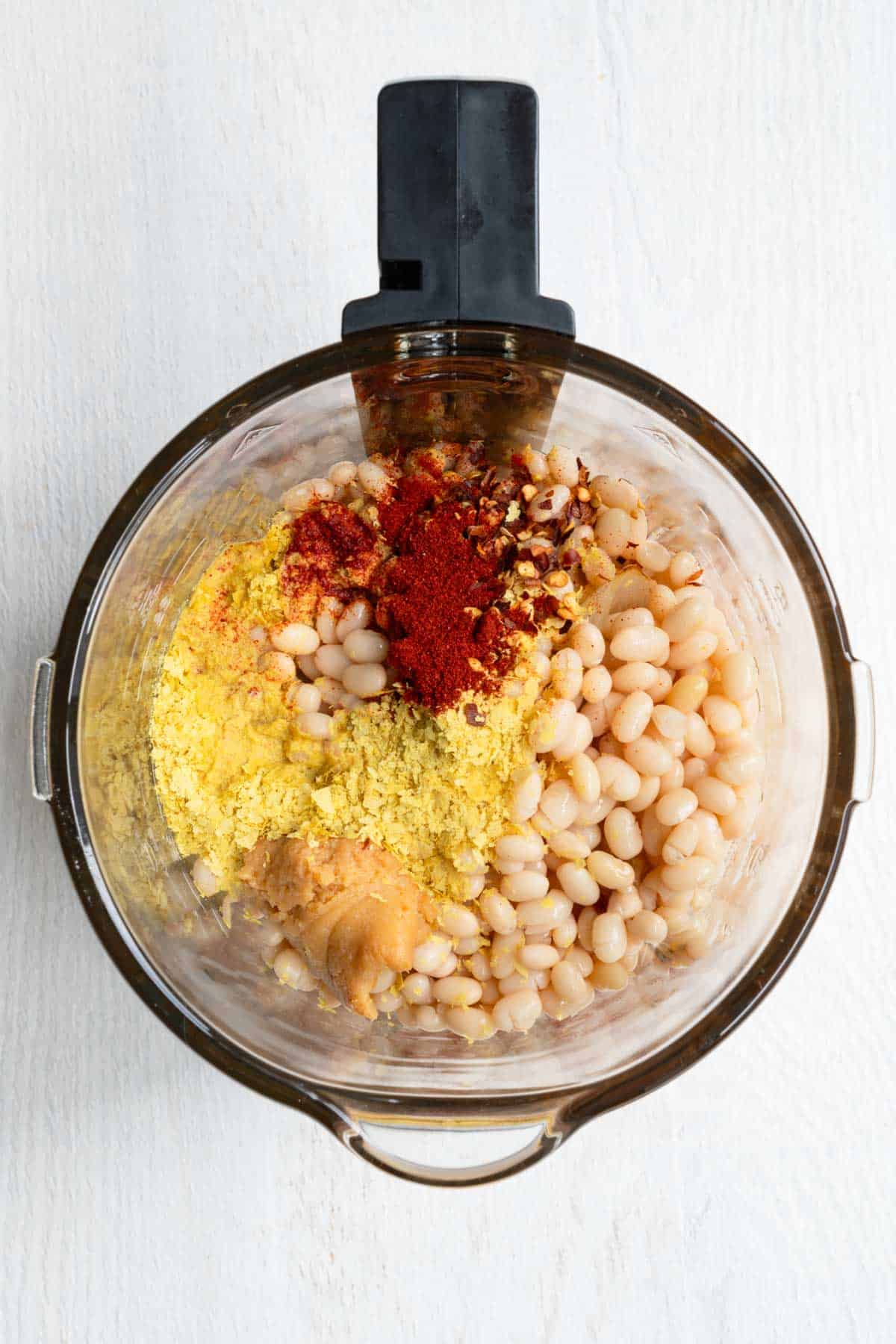 White beans, miso, squash, nutritional yeast, spices, chili flakes, tomatoes, broth, onion, garlic, and fresh herbs in the canister of a blender.