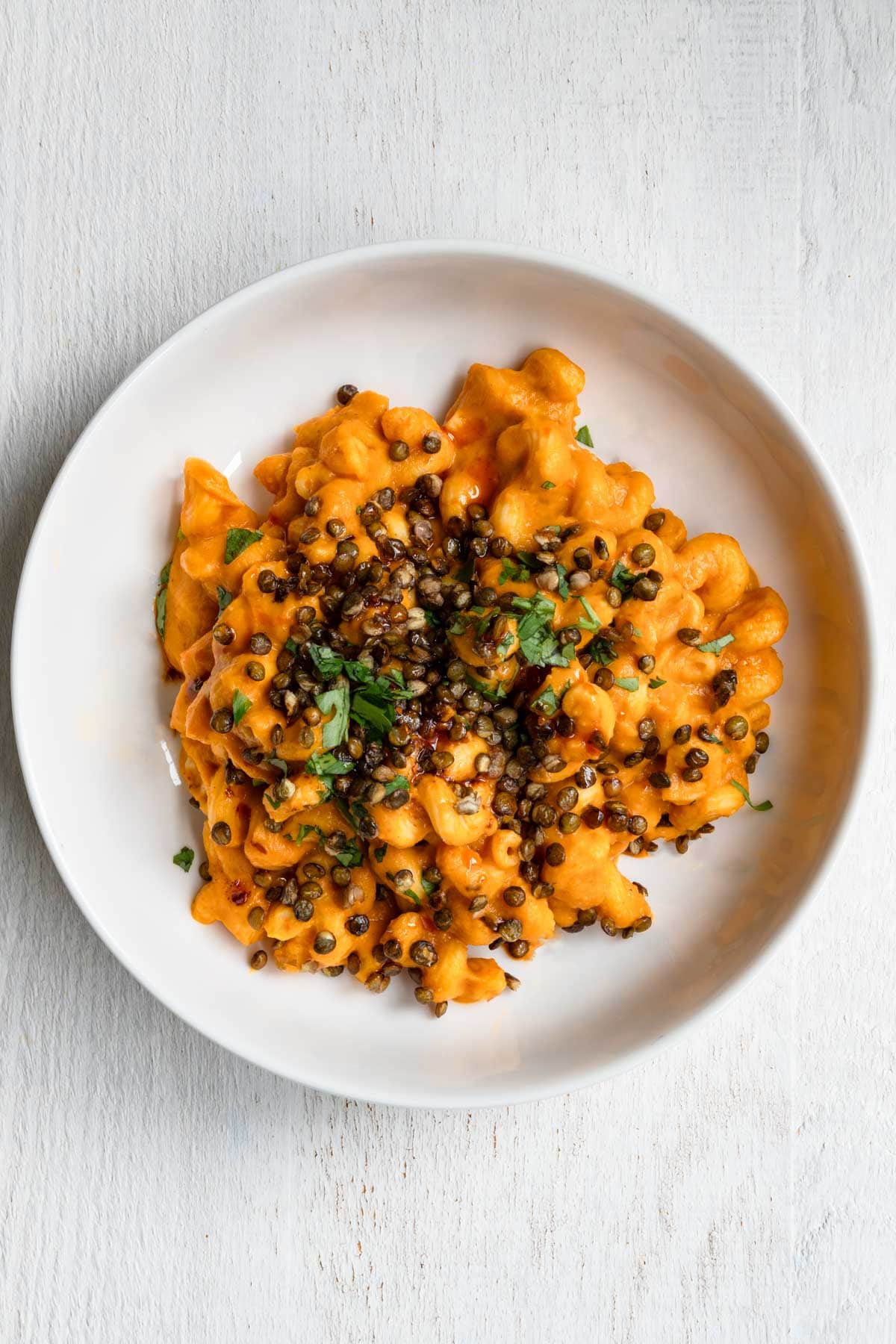 Creamy butternut squash pasta sauce with pasta in a bowl topped with roasted lentils and chili sauce.