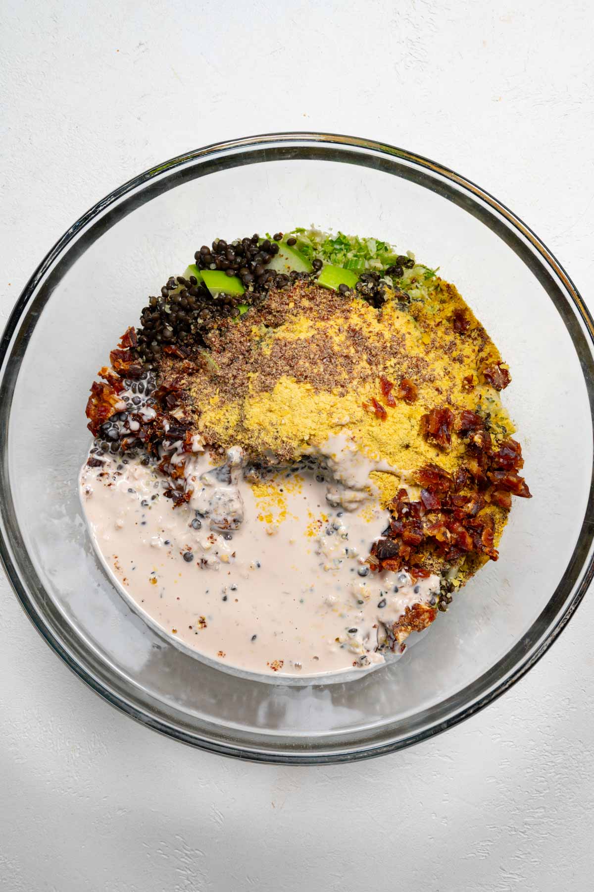 Lentils, creamy dressing, chopped dates, nutritional yeast, celery, apple, and shaved Brussels sprouts in a glass bowl.