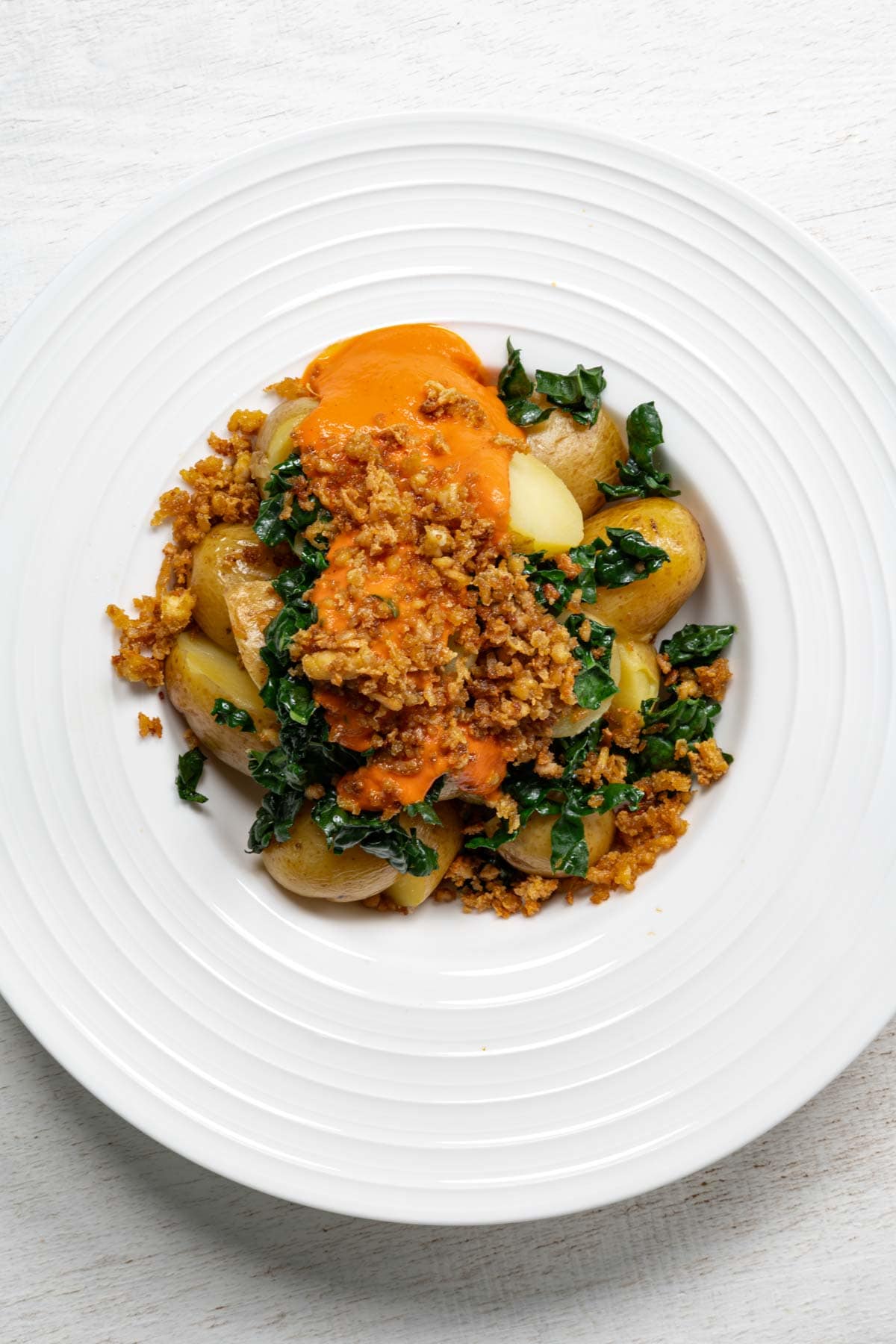 Loaded potato bowl with sliced baby potatoes, tofu crumbles, chopped kale, and red sauce in white bowls.