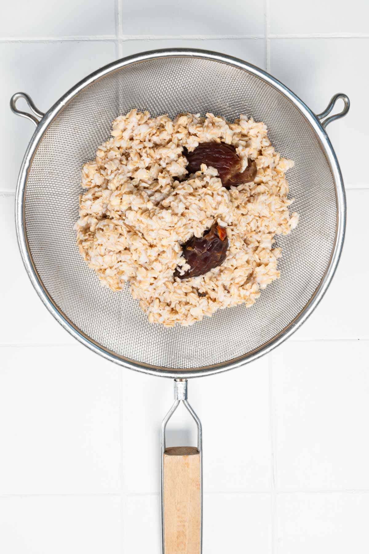 Drained soaked oats and dates in a fine mesh sieve.