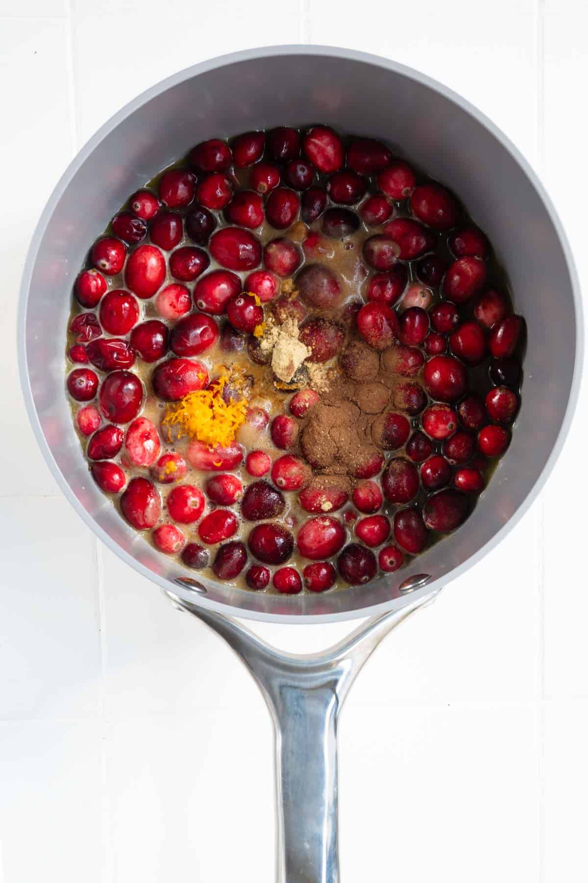 Fresh whole cranberries, date paste, ground cinnamon, ground ginger, orange juice, and orange zest in a saucepan.
