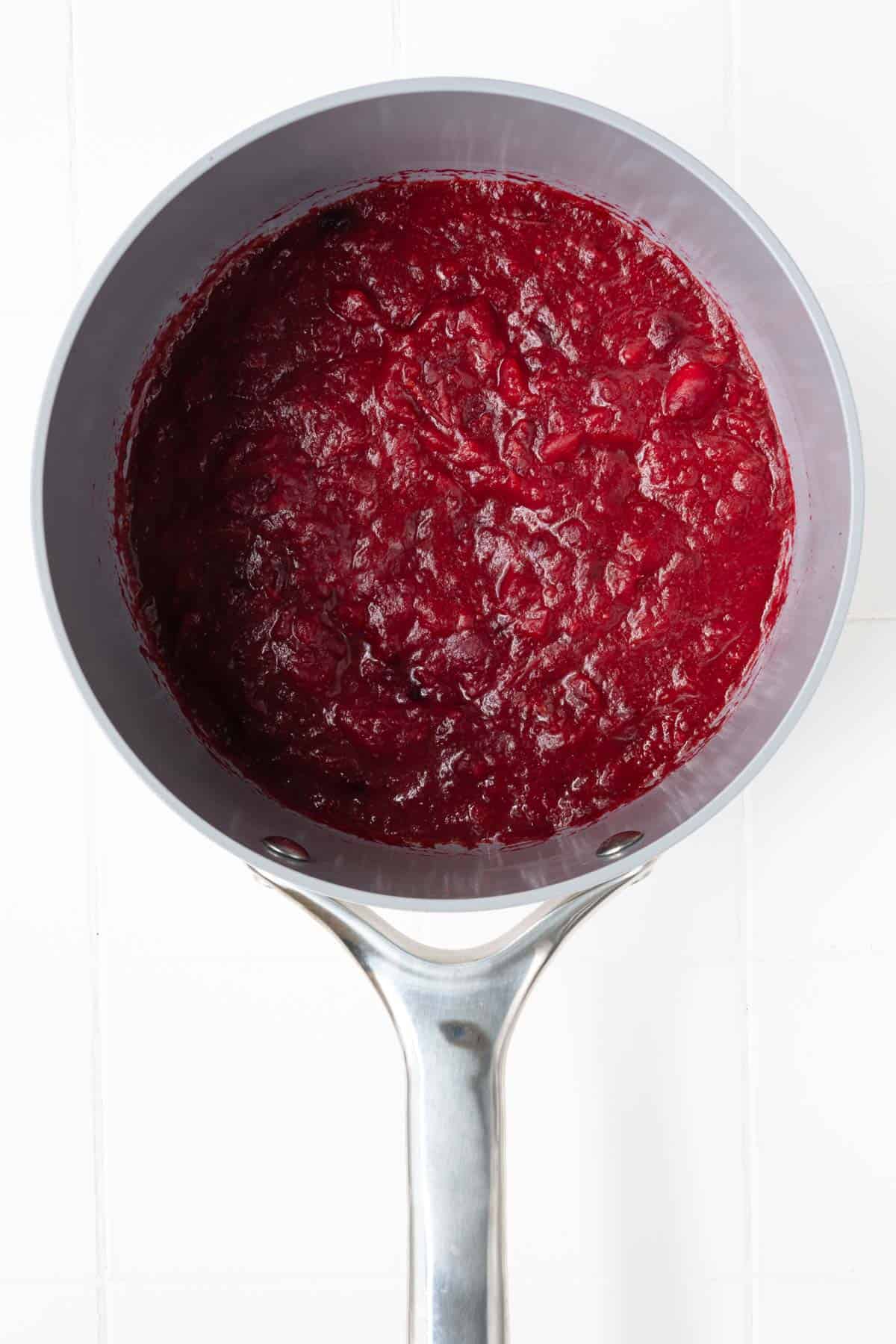 Red cranberries cooking in orange juice and date paste with seasonings in a saucepan.