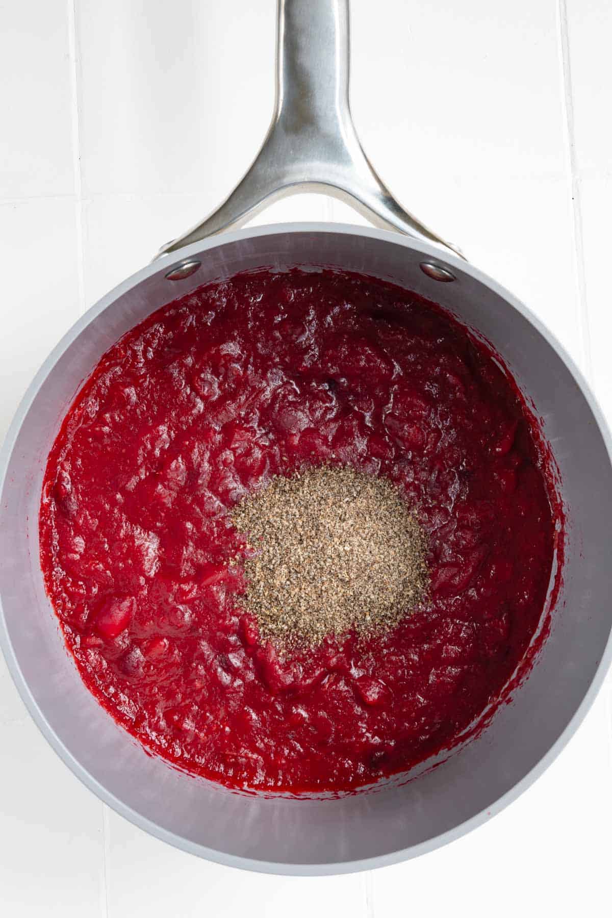 Red cranberries cooking in orange juice and date paste with seasonings and a spoonful of ground chia seeds on top.