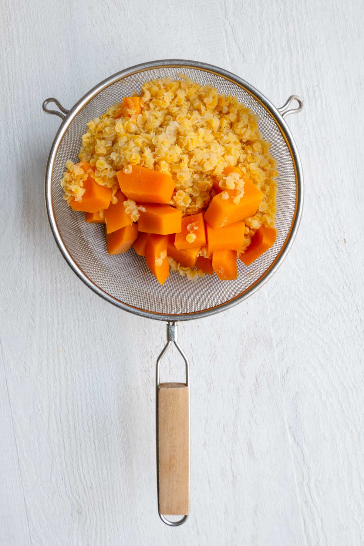 Cooked butternut squash and red lentils in a fine-mesh sieve.