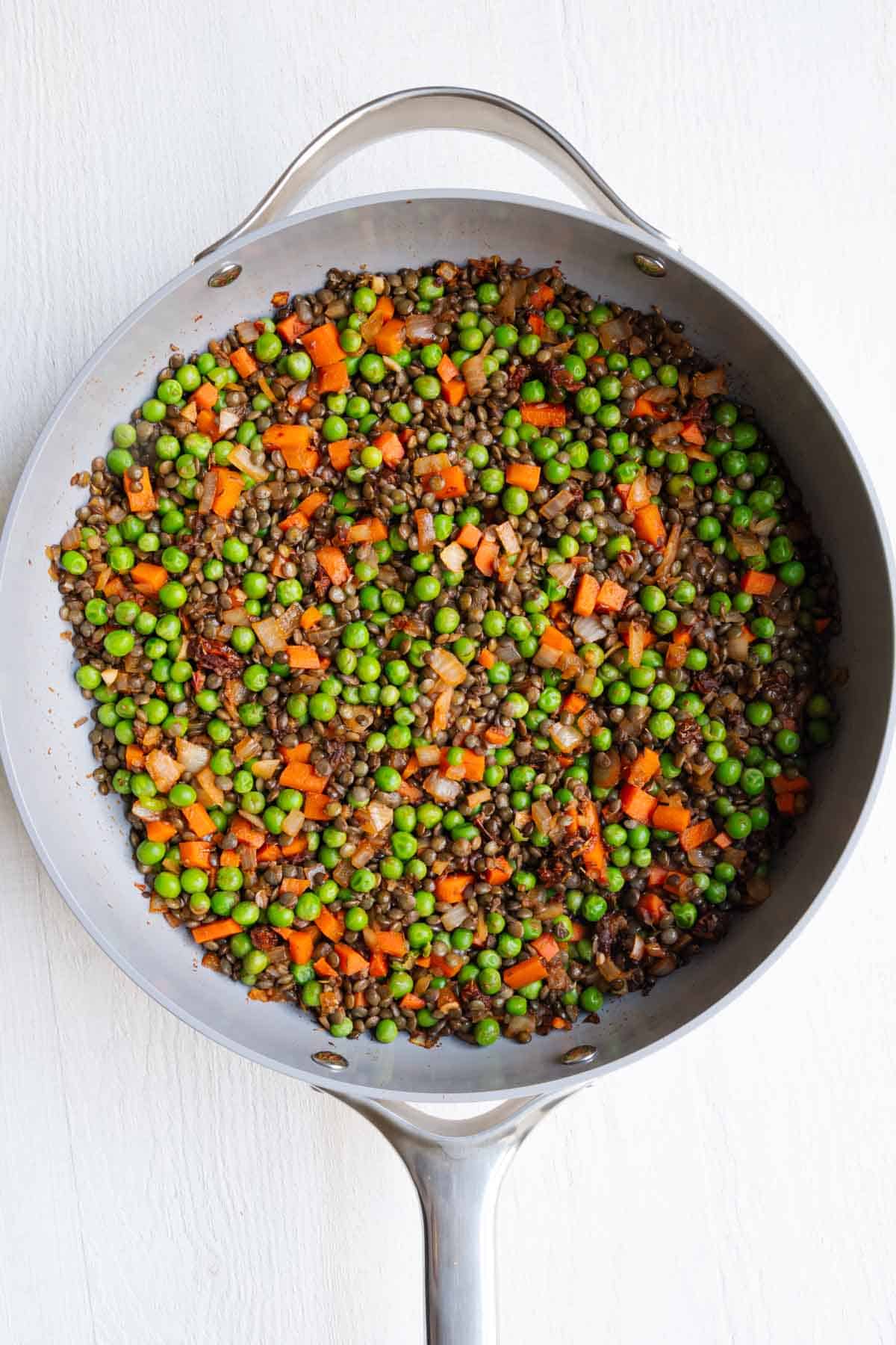 Cooked lentils, green peas, carrots, onion, garlic, and seasoning in a saucepan.