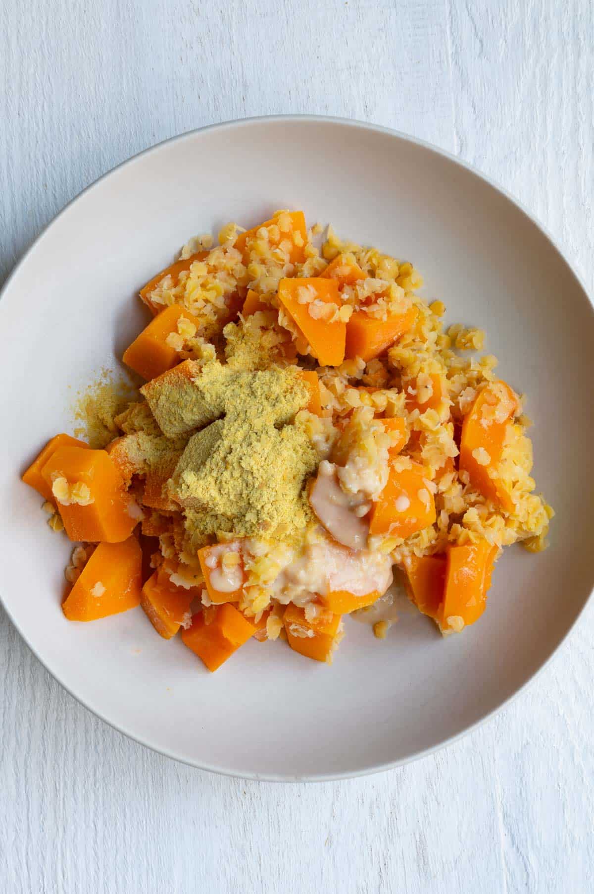 Cooked butternut squash cubes and red lentils topped with miso, nondairy milk, tahini, and nutritional yeast.