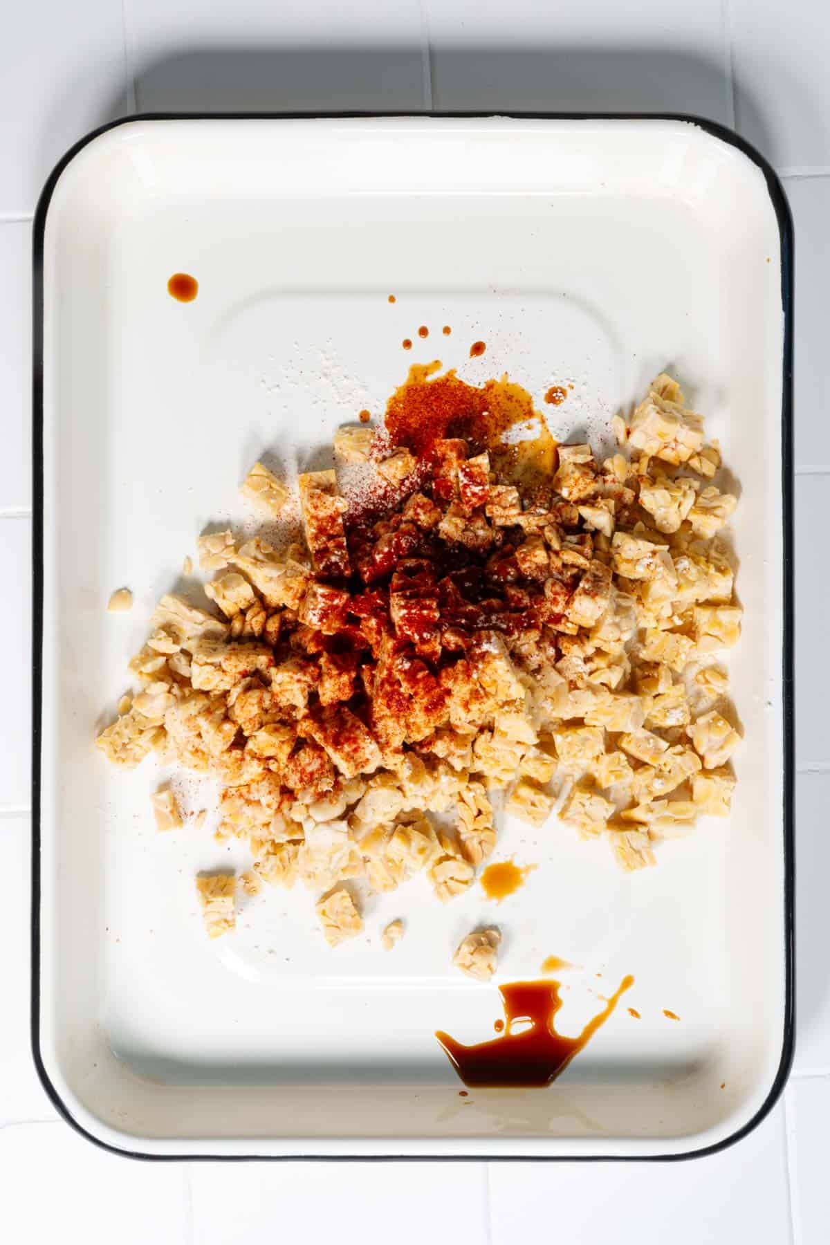 Cubed tempeh on a baking sheet seasoned with smoked paprika, garlic powder, and coconut aminos.