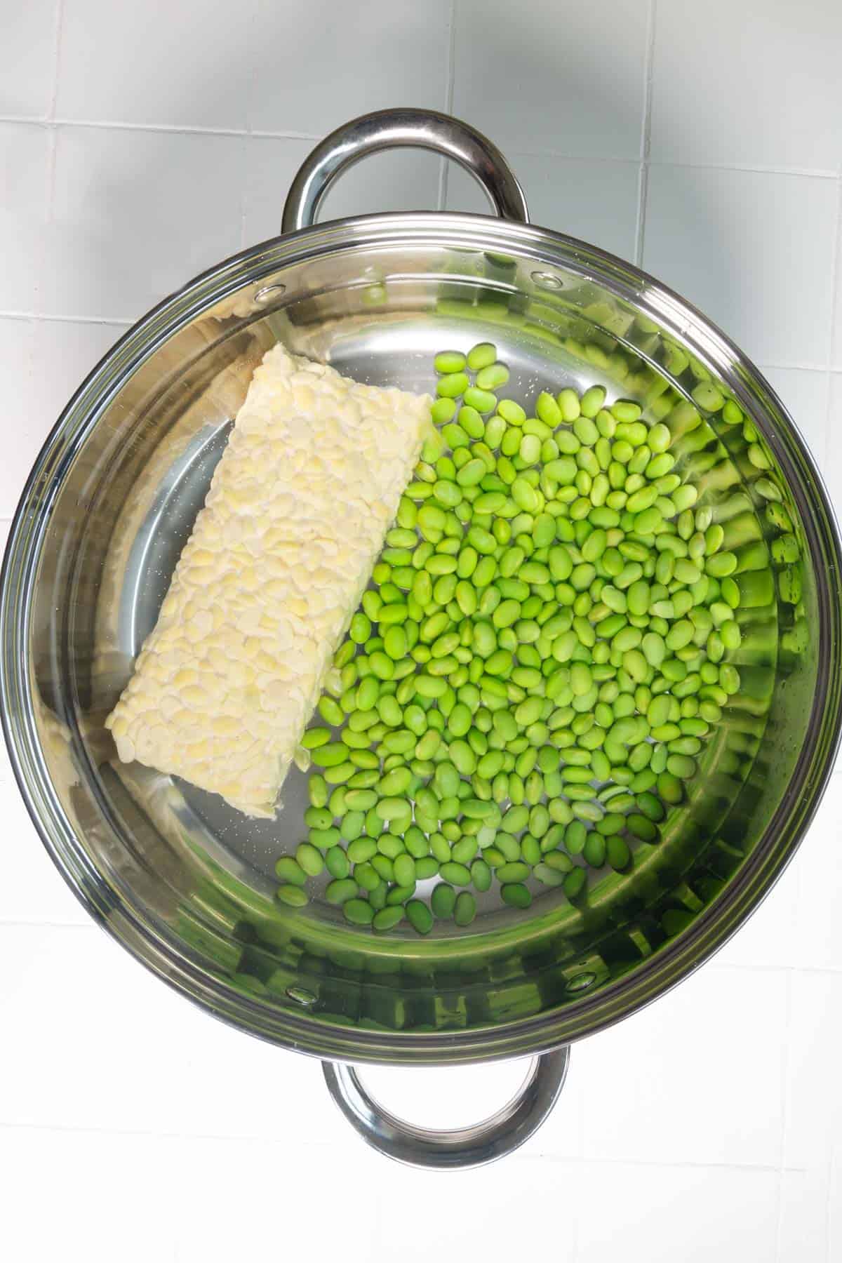 Edamame and tempeh simmering in a stainless steel saucepan.
