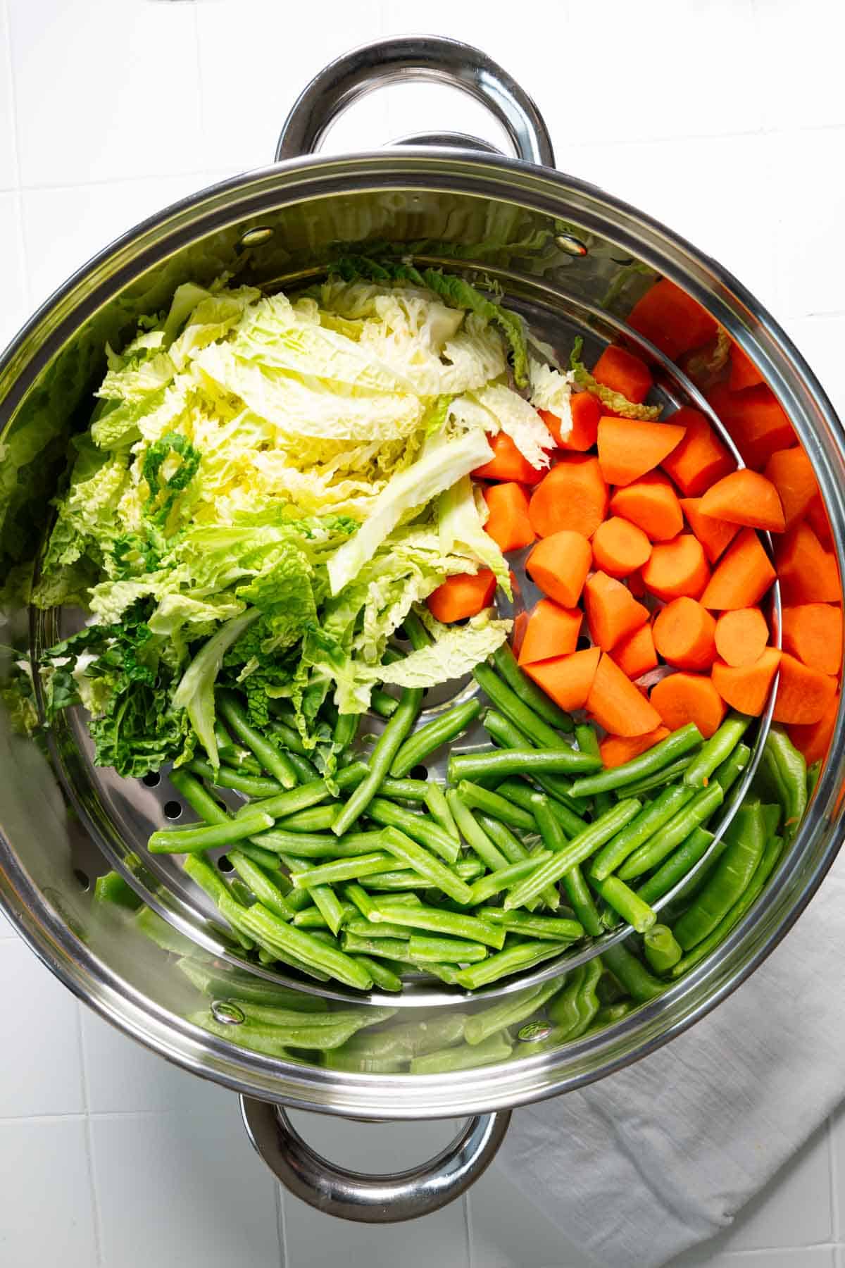 Carrots, napa cabbage, and green beans in a metal steamer basket.