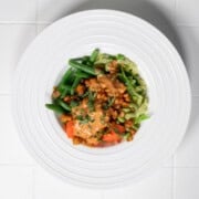 Steamed vegetable bowl with carrots, cabbage, edamame, tempeh, green beans, and peanut sauce in a white bowl.
