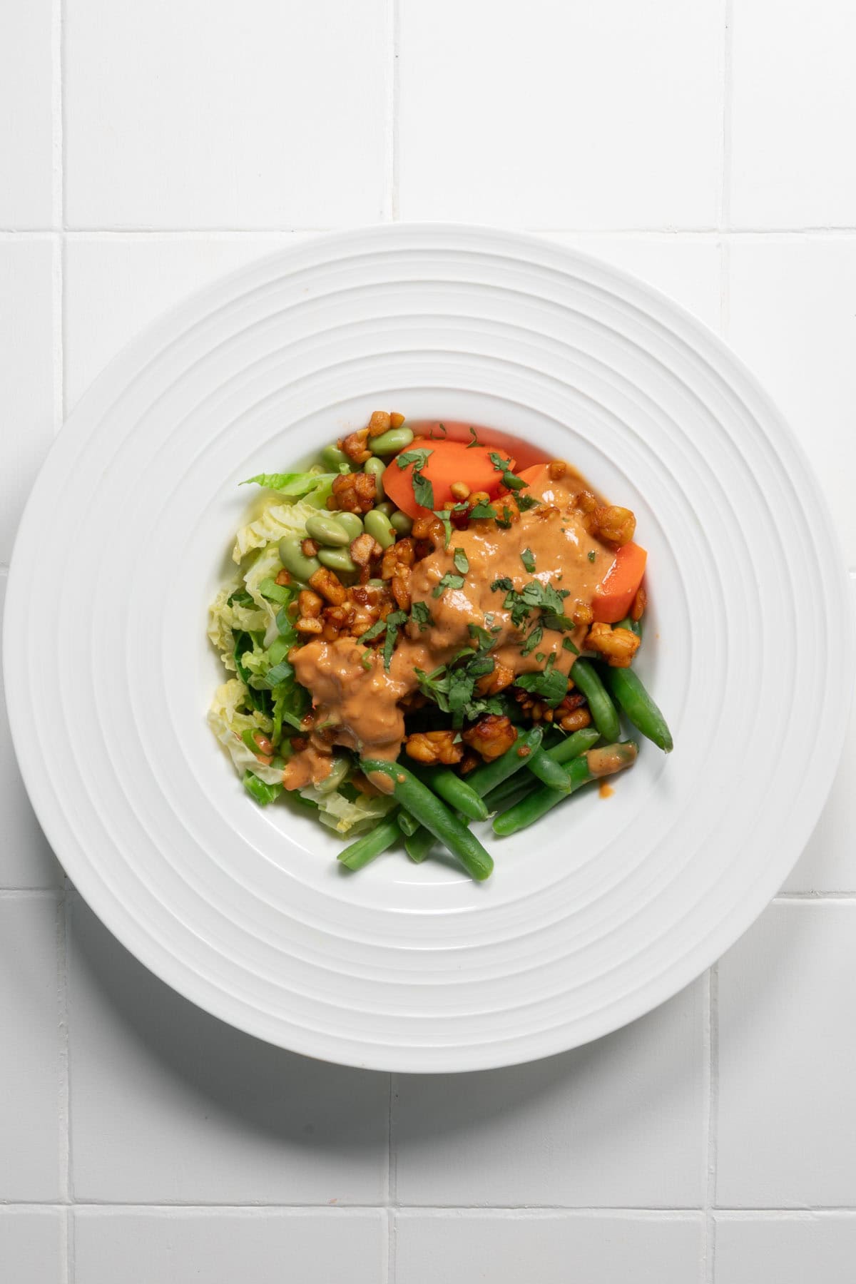 Steamed vegetable bowl with carrots, cabbage, edamame, tempeh, green beans, and peanut sauce.