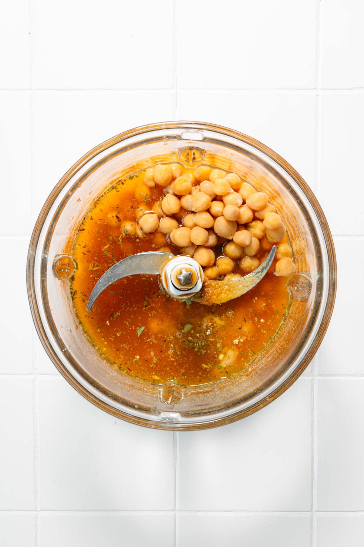 Chickpeas, vegetable broth, and seasoning in the canister of a food processor.