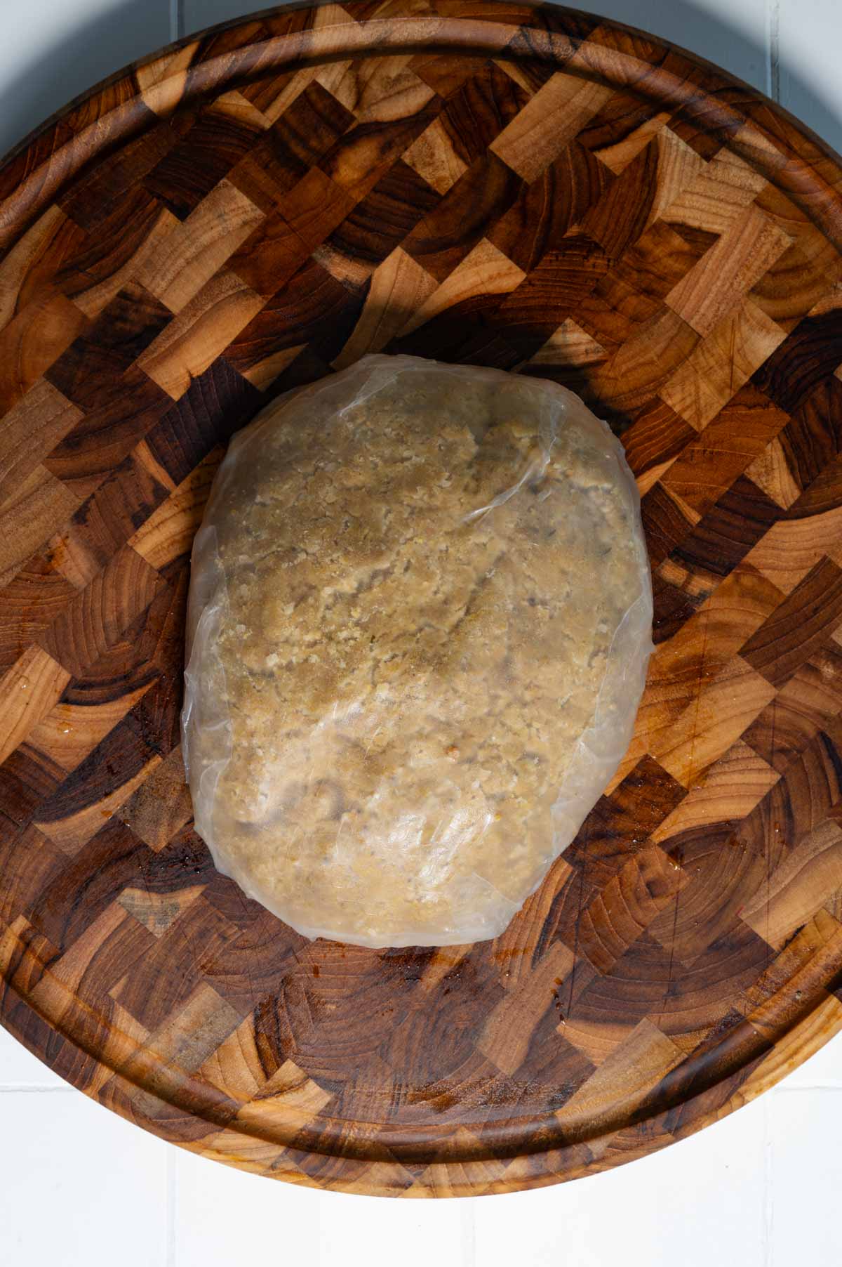 Oval shaped dough wrapped in rice paper on a wooden cutting board.