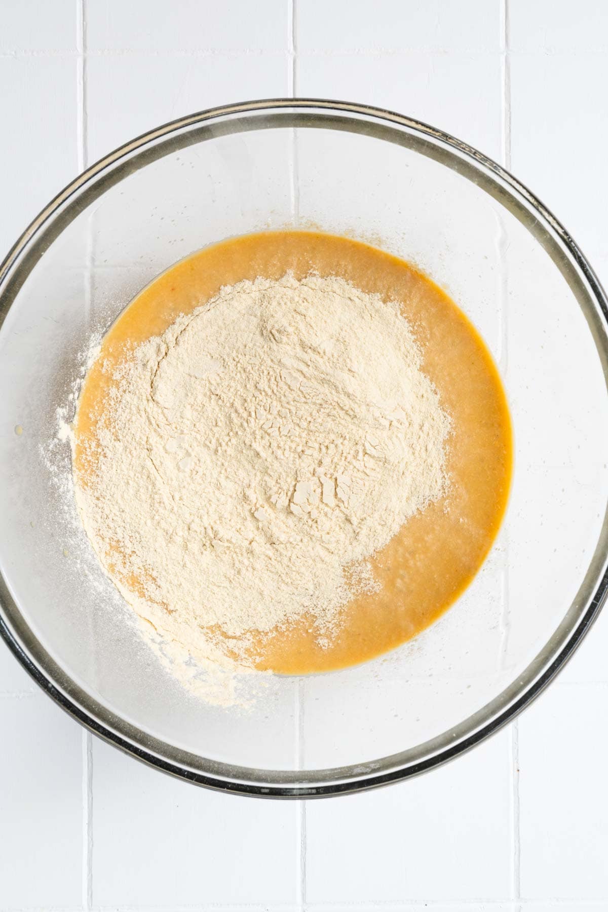 Blended chickpeas, broth, and seasoning in a large glass bowl with vital wheat gluten flour.