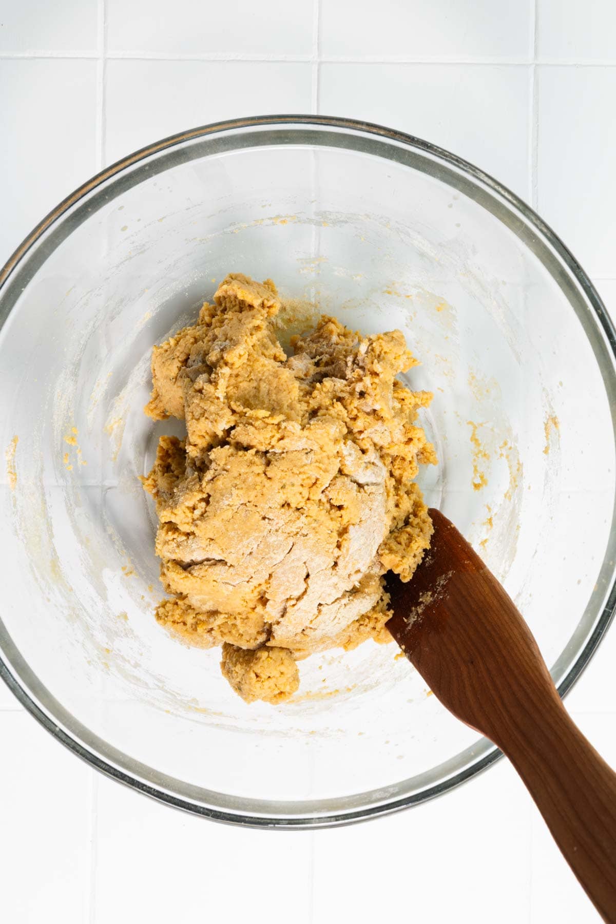 Vital wheat gluten dough in a large glass bowl with a wooden spatula.