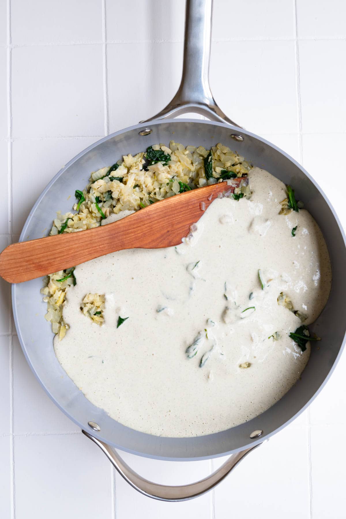 Chopped artichokes and wilted spinach in a skillet with creamy vegan white sauce.