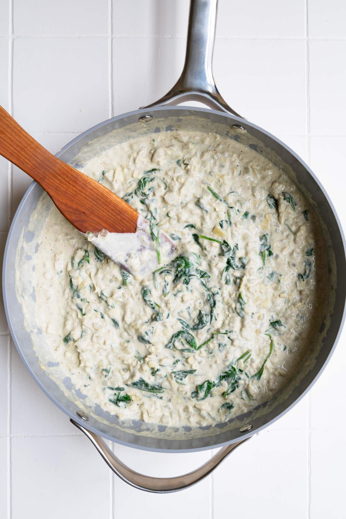 Vegan spinach and artichoke dip cooking in a steel skillet.