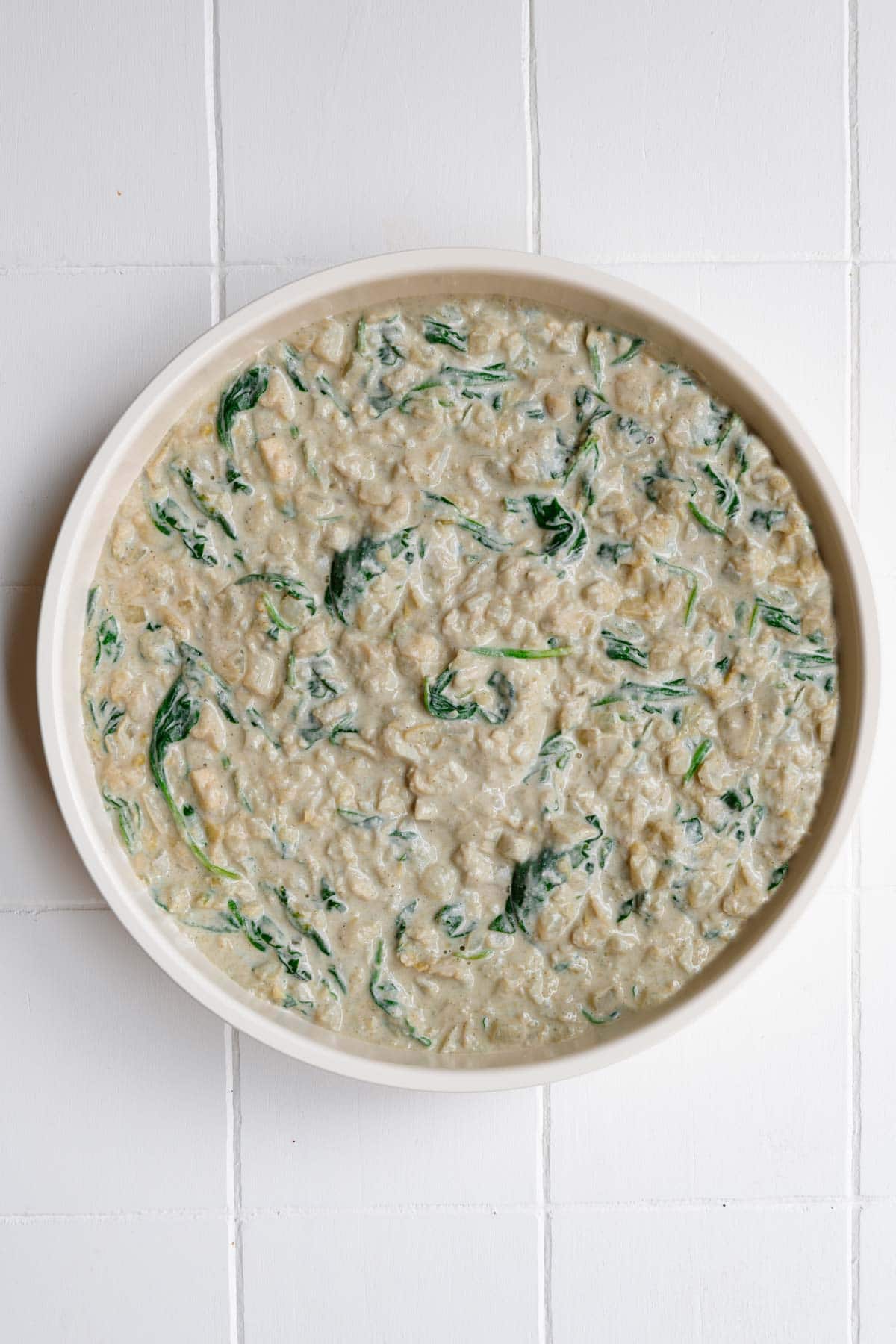 Artichokes and spinach in a vegan creamy sauce ready to bake in a round baking dish.
