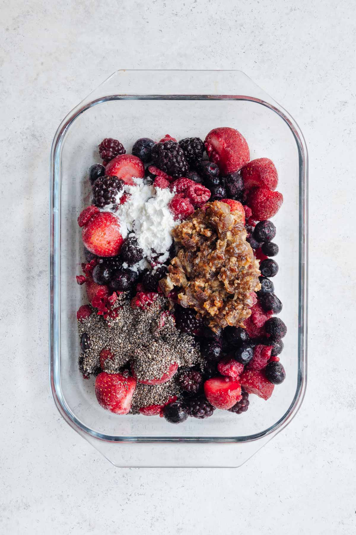 Mixed triple berries, chopped dates, chia seeds, arrowroot, and lemon juice in a baking dish.