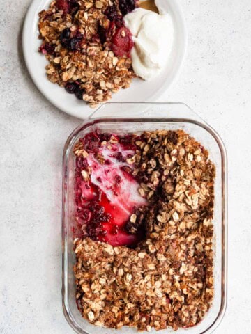 Gluten-free berry crisp with no added sugar in a glass baking dish and a serving on a white plate with yogurt.