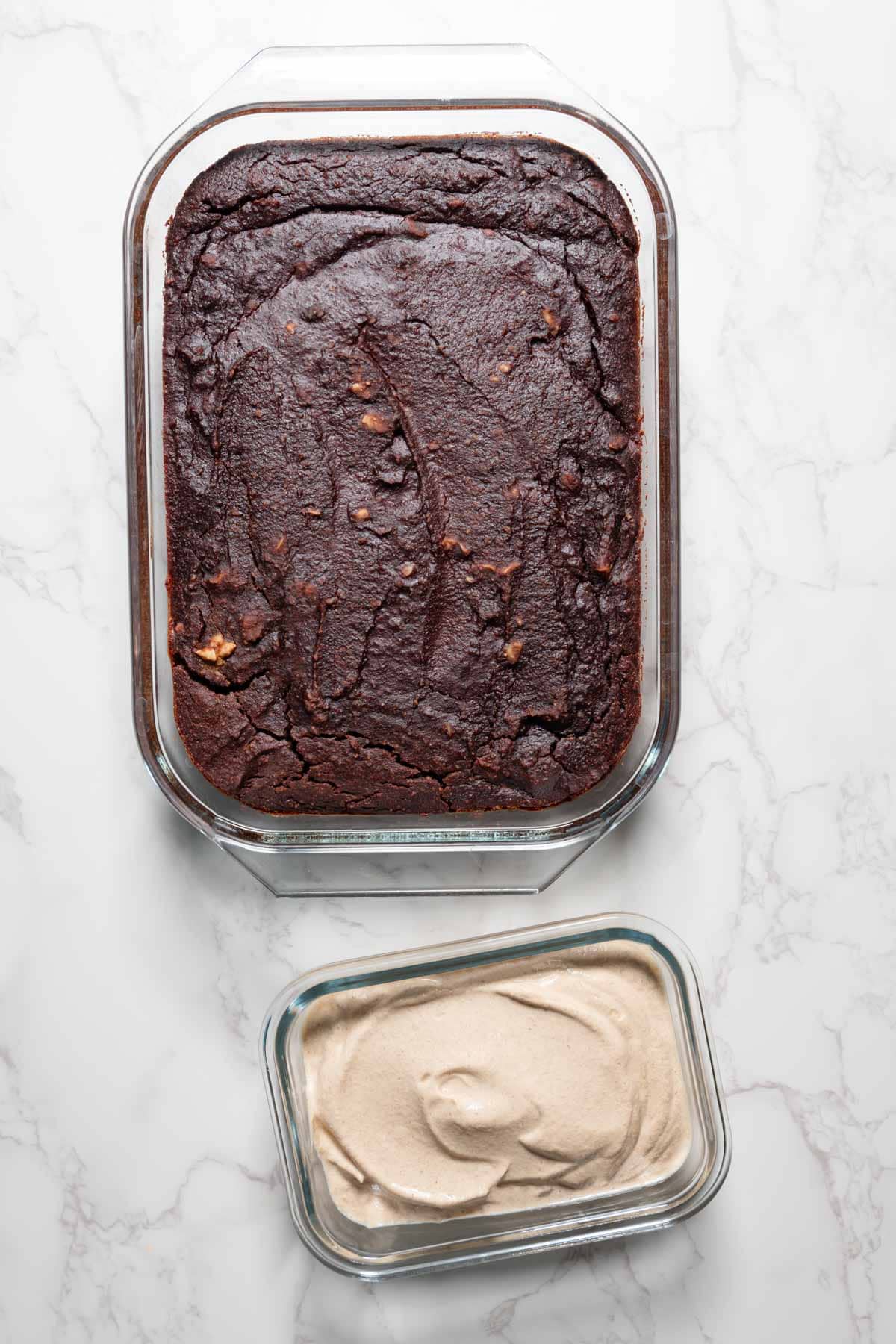 Black bean brownies in a glass baking dish next to a container of walnut cream frosting.