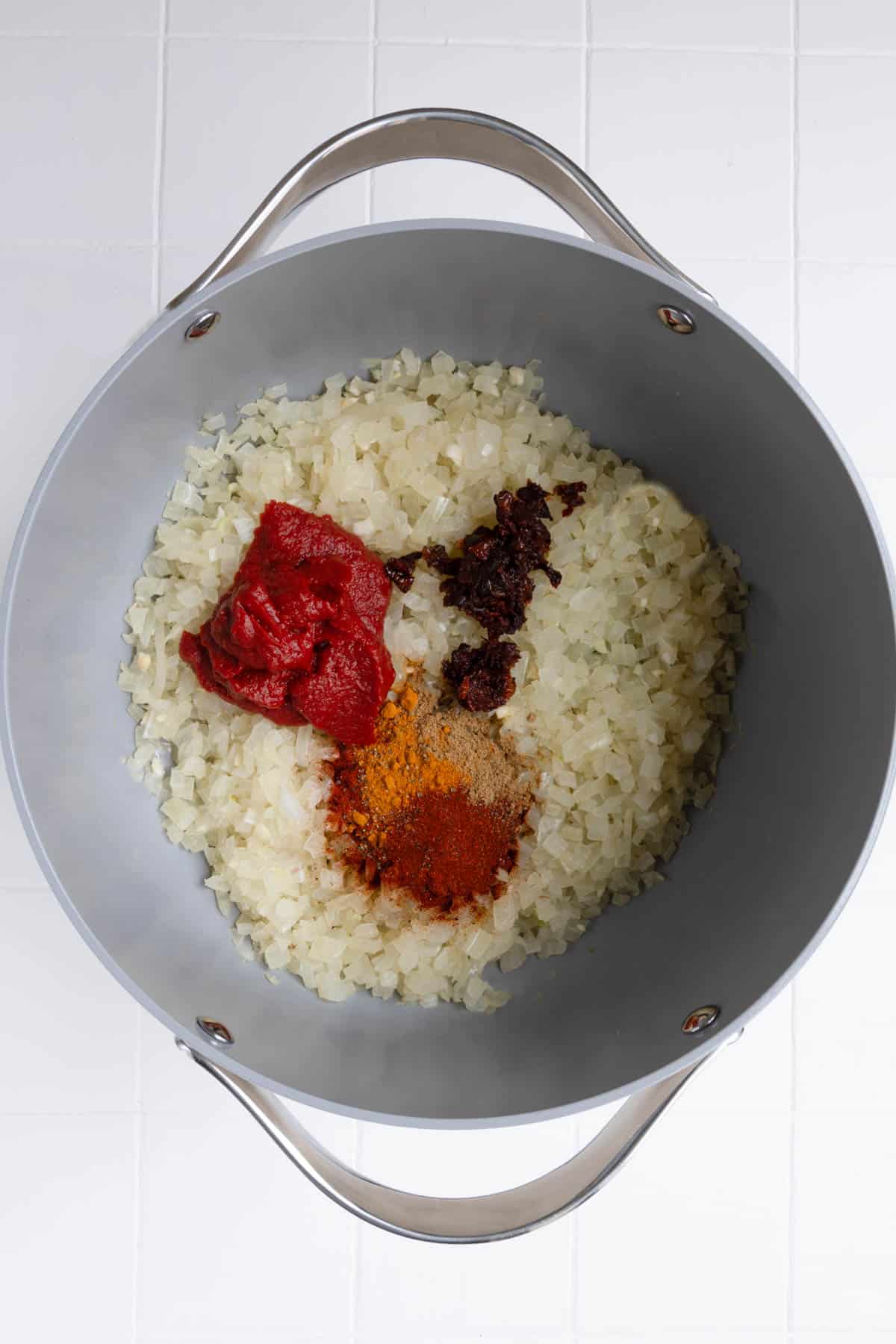 Cooked onion, tomato paste, seasoning, and sun-dried tomatoes in a saucepan.