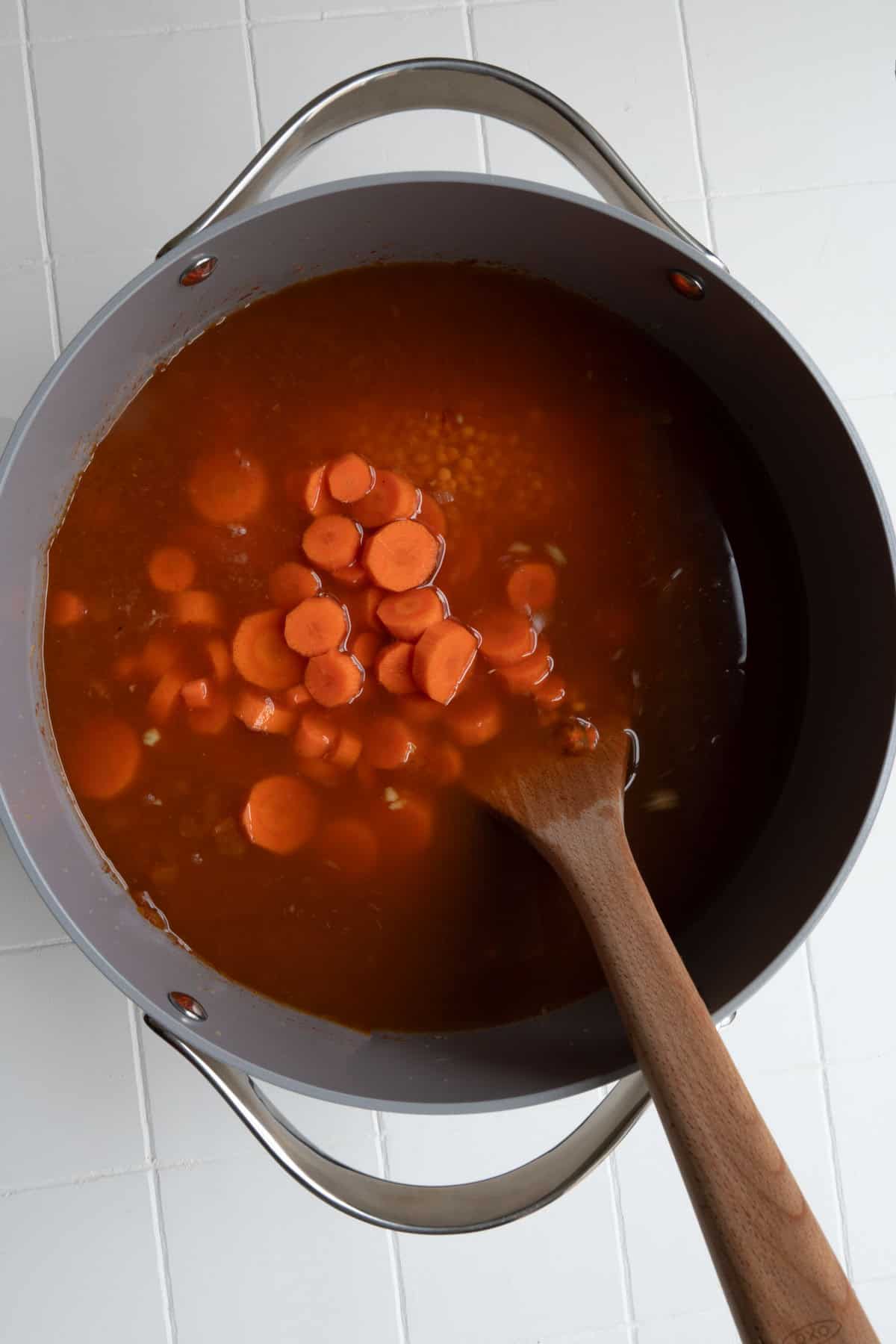 Vegetable broth, red lentils, aromatics, seasoning, and carrots cooking.