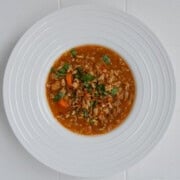 Tomato lentil soup with tofu cream and crumbled tofu in a white bowl.