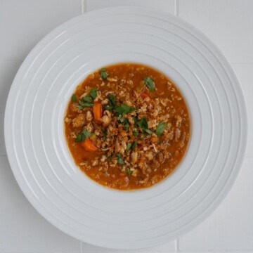 Tomato lentil soup with tofu cream and crumbled tofu in a white bowl.