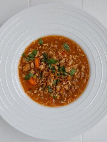 Tomato lentil soup with tofu cream and crumbled tofu in a white bowl.