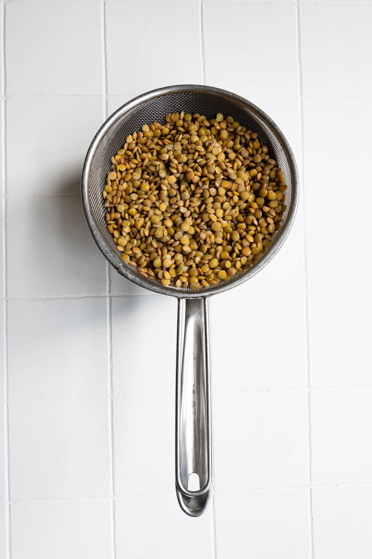 Cooked and drained green lentils in a fine mesh sieve.