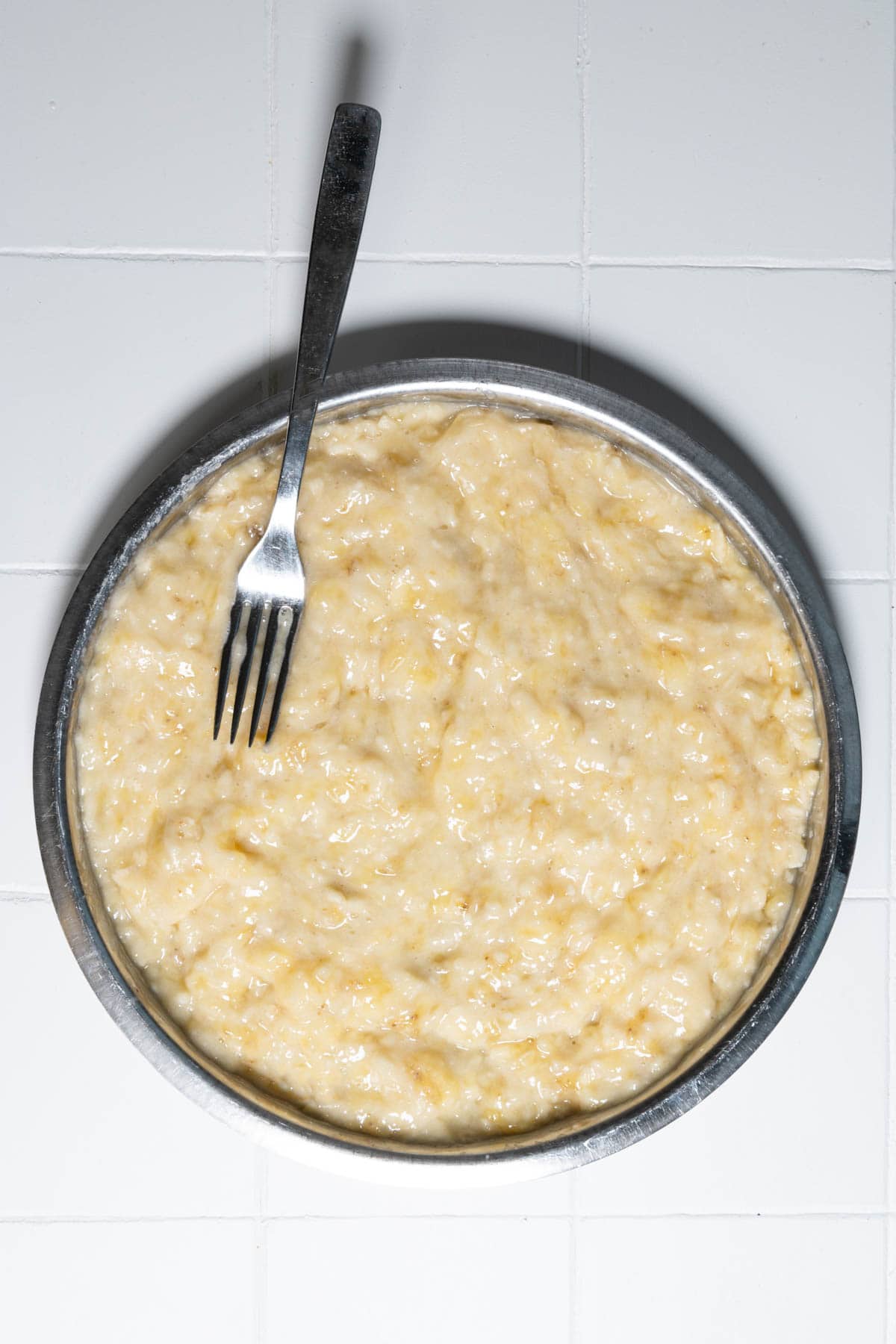 Mashed banana with a fork on a metal plate.