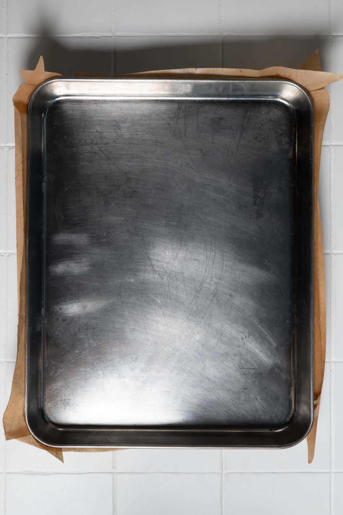 A metal baking sheet on parchment paper pressing down the granola batter.