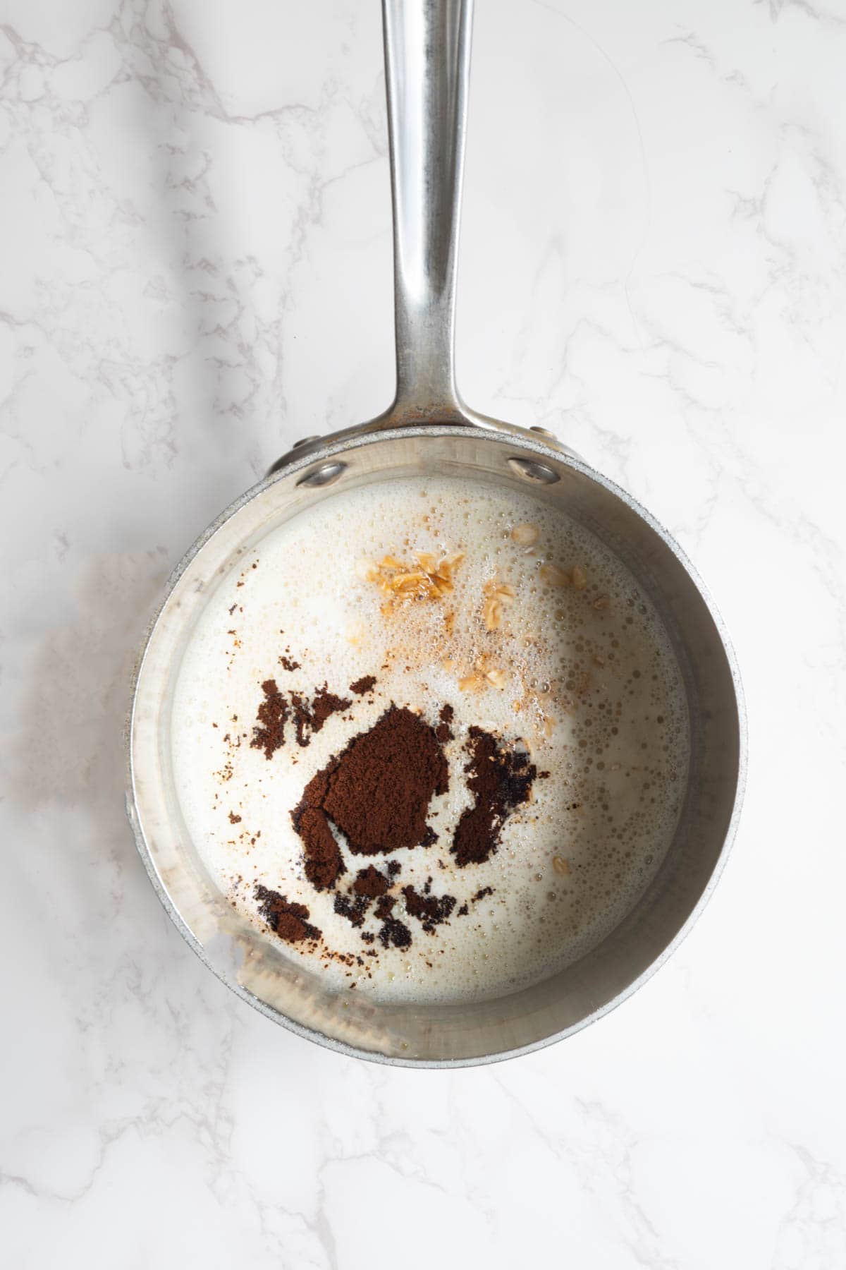 Nondairy milk, rolled oats, and espresso powder in a stainless steel saucepan.