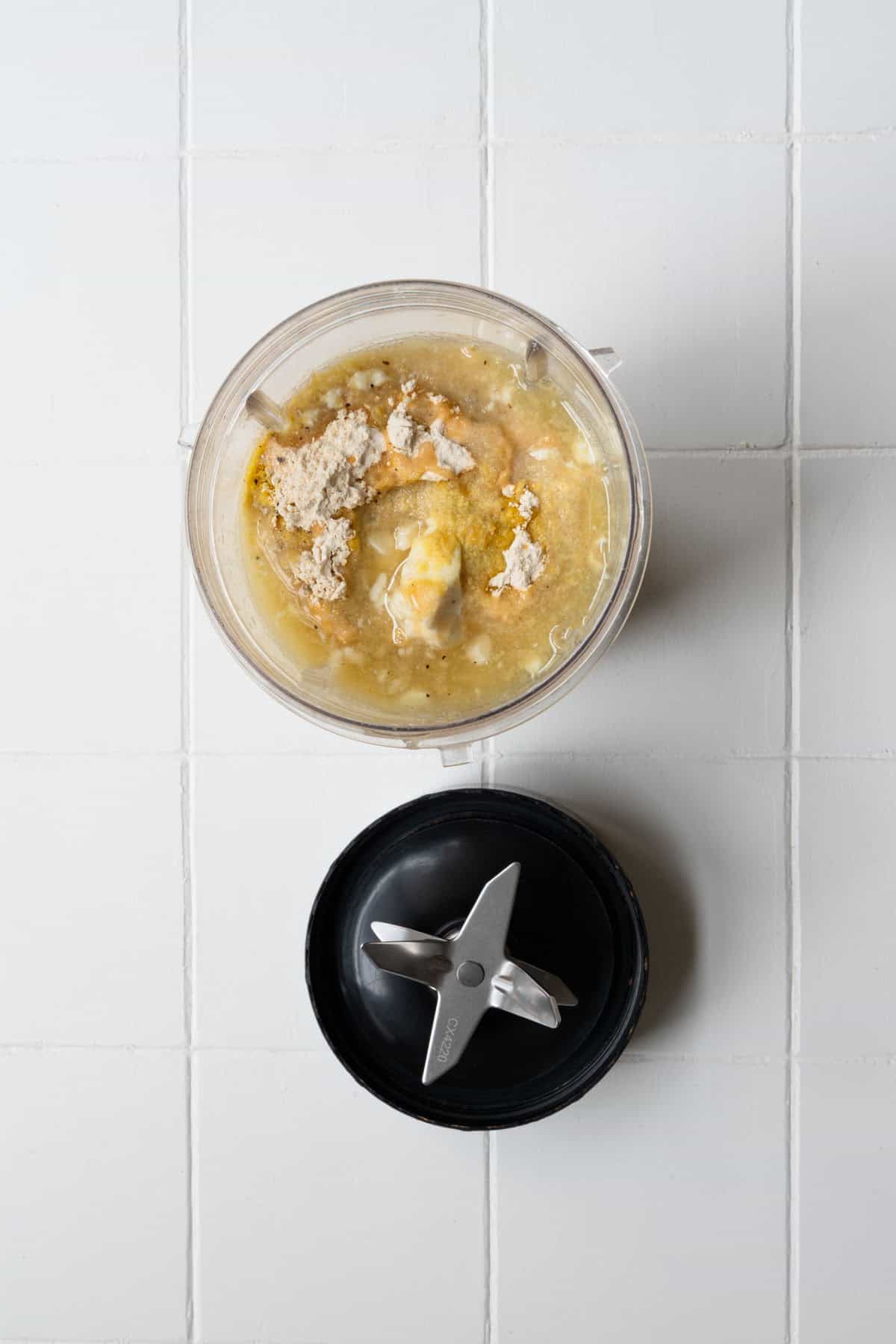 Silken tofu, nutritional yeast, lemon juice, and seasonings in the canister of a blender.