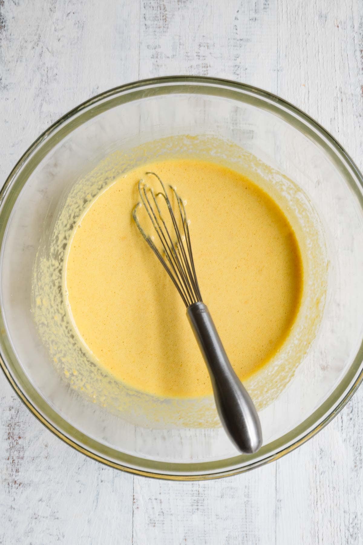 Yellow liquid mixture in a bowl with a whisk.